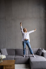 Young woman dancing with headphones and relax at home. Happy woman with smartphone on sofa in living room