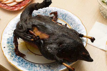 Burnt bird carcass on serving plate on dining table. Serve charred spoiled dish. Lousy housewife...