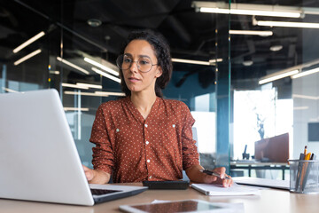 Successful satisfied and happy business woman working inside modern office, hispanic woman in...