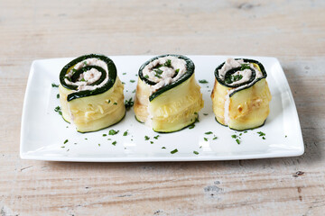 Grilled zucchini rolls stuffed with cream cheese and tuna on wooden table