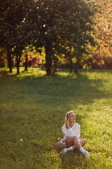 Young blonde girl is wearing a white hoodie smiling and walking in the woods