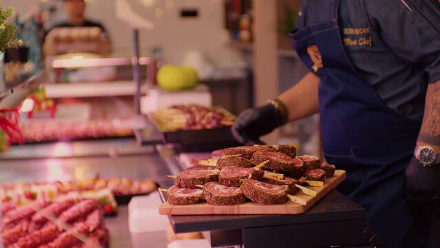Butcher bringing pre-cut slices of homemade sausege and barbecue preps on skewers. Fulfilling the gaps with new arrivals.