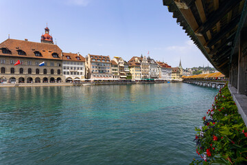 Obraz premium LUCERNE, SWITZERLAND, JUNE 21, 2022 - View of the wodden covered Kapellbrucke Bridge on the Reuss river and buildings in city center of Lucerne, Switzerland