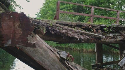Fototapeta na wymiar Old Damaged Collapsed Wooden Bridge over Shallow River 