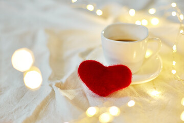 Valentine's Day Cup of coffee in bed with a red hearts and lights, copy space. Greeting card, romantic breakfast.