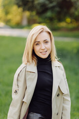 Caucasian blonde woman wearind trench smile happily on sunny spring day outside walking in park