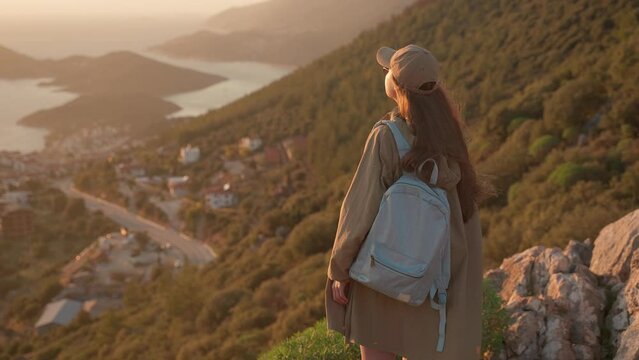 A young woman stands on a viewpoint and admires the view of a coastal city in Turkey. The tourist destination is Kash, Turkey.