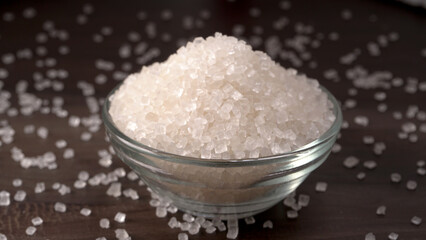 Bowl and spoon with sugar on wooden background.