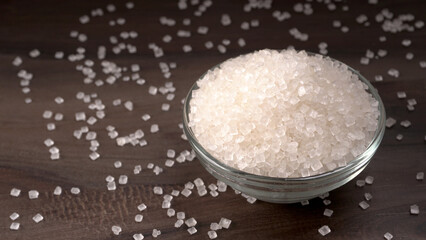 Bowl and spoon with sugar on wooden background.