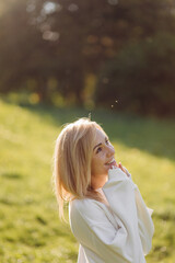 Young blonde girl is wearing a white hoodie smiling and walking in the woods