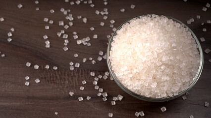 Bowl and spoon with sugar on wooden background.