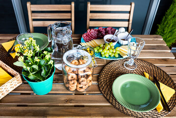 Rustic outdoor table with taralli and flower plant in the middle while a delicious plate with salami and cheese lies on the side. Tasty dish with pepperoni, cheese and green grape on a homely board