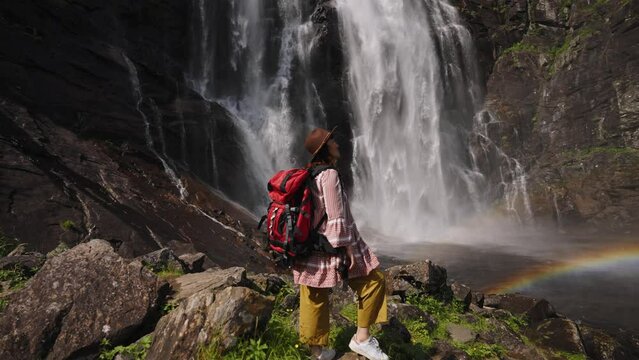Girl standing with backpack observing a forest landscape with waterfall. woman in front of a waterfall enjoying the nature. Active turism norway