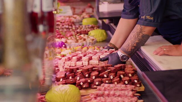 Butcher hands in gloves placing a tray full of pieces of meat on skewers. Butchery worker fulfilling the gaps with pregessed meat.