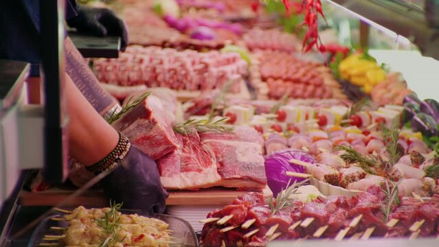 Butchers hands with black gloves putting hunks of fresh meat on display. Meat departmdent with raw fresh meat for sale.