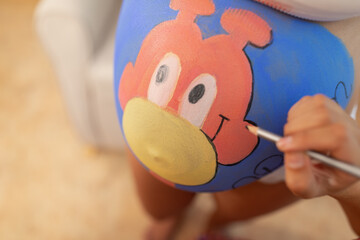 Close up view of a bodypainting artist's work on a pregnant woman's belly at her home