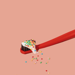 Red toothbrush with toothpaste decorated with colorful sugar sprinkles on pink background with copy space. Dental medical Christmas and New Year concept. Creative flat lay and still life.