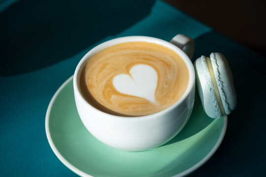 Cup of cappuccino with heart and macaron on green table