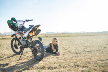 Plakat Beautiful woman in motorcycle outfit. Female motocross racer next to her motorcycle. female motorcycle rider, motorbike rider travel the world, girl resting, freedom lifestyle