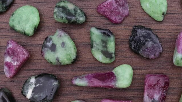 Ruby zoisite rare jewel stones texture on brown varnished wood background. Moving right seamless loop backdrop.