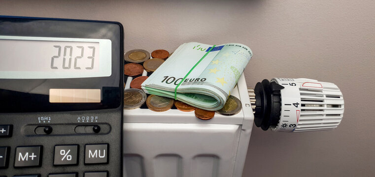 The prospect of growth in the cost of heating in the new 2023. Calculator near the battery of a heating radiator with a thermostat. There are a lot of coins on the radiator