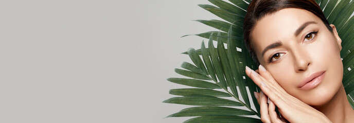 Organic Beauty and Skincare Concept. Closeup natural woman face with fresh hydrated and glowing skin against green exotic leaves