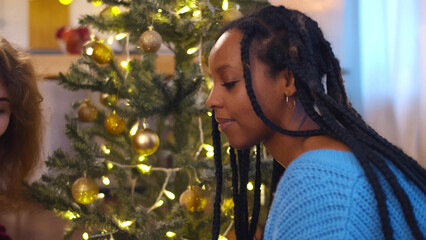Diverse lesbian couple putting gift boxes under christmas tree