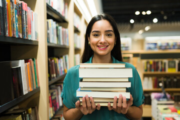 Hispanic woman looking happy carrying a lot of books at the bookstore