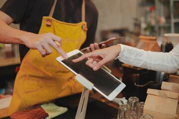 Barista and customer are pointing at digital tablet or black screen. Customer is ordering by a...