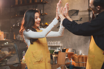 A postitive barista, staff or waitress and waiter give high five with both hands with the successful result or target. Concept of cheerful, frienship co-worker, celebrate at coffee shop and bakery.