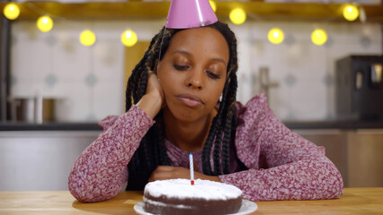 Sad young African-American woman celebrating birthday alone during pandemic.