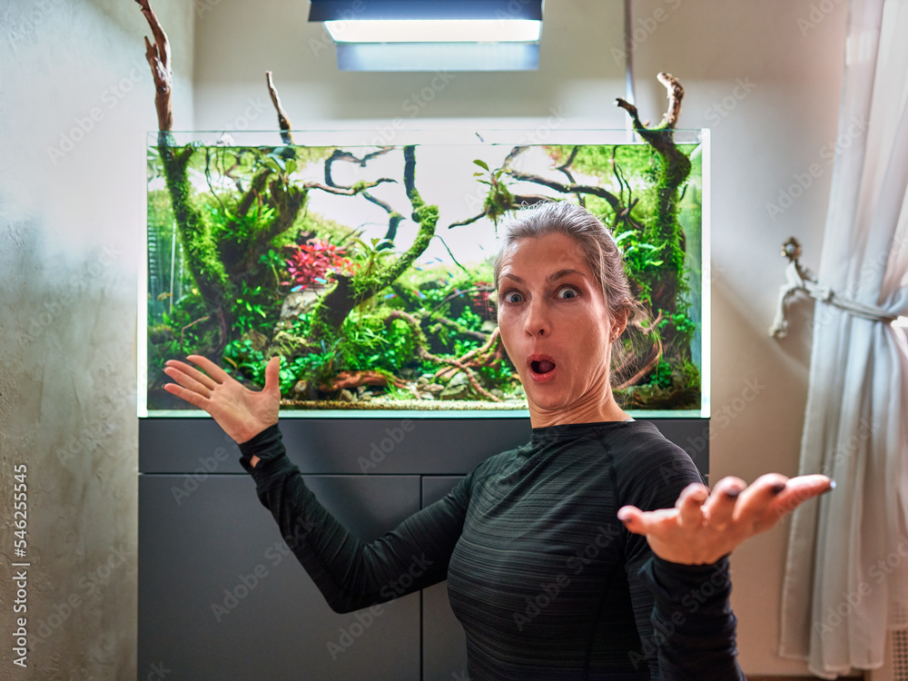 Wall mural a beautiful very surprised emotional woman in front of aquarium aquascape.