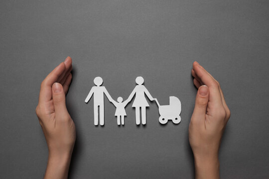 Woman protecting paper family figures on grey background, top view. Insurance concept