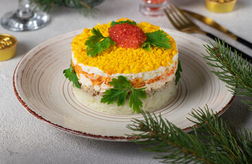 Festive puff salad Mimosa with canned fish, potatoes, cheese, carrots and eggs, garnished with red caviar and parsley leaves