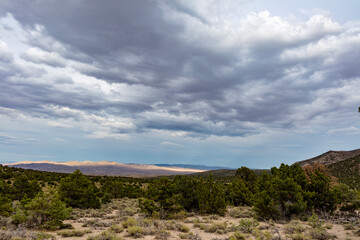 Rain clouds gather on a summer  evening over the Great Basin Desert and Shrublands south of Baker, Nevada near the Utah Border. Rays of sunlight breaking through clouds illuminate a distance mountain.