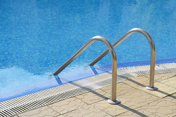 Outdoor swimming pool with ladder and handrails on sunny day