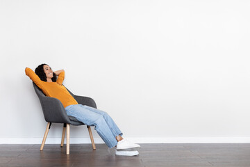 Relaxed young woman reclining in arm chair over white wall