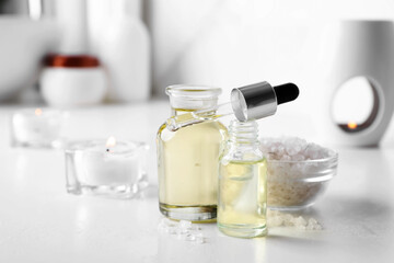 Essential oils, sea salt and candles on white table in bathroom, closeup