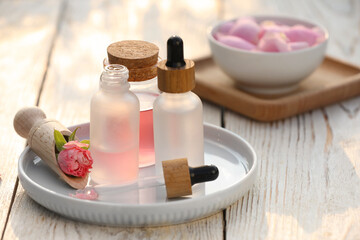 Fototapeta na wymiar Bottles of rose essential oil and flowers on white wooden table