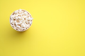 Paper cup with delicious popcorn on yellow background, top view. Space for text