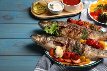 Plate with delicious baked sea bass fish and vegetables on light blue table