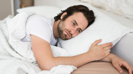 Tired sad depressed millennial caucasian man with stubble cant fall asleep in white bed, suffer from health problems - obrazy, fototapety, plakaty