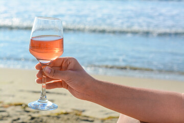 Woman with glass of tasty rose wine near sea, closeup