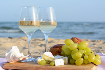 Glasses with white wine and snacks for beach picnic on sandy seashore