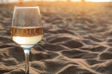 Glass of tasty wine on sandy beach, space for text
