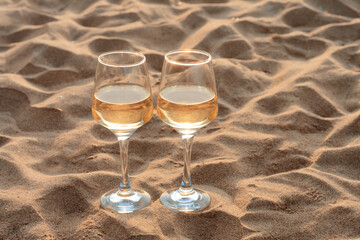 Glasses of tasty wine on sand, space for text