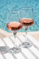 Glasses of tasty rose wine on white wooden table near swimming pool, closeup