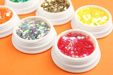 Jars with colorful shiny glitter on orange background, closeup