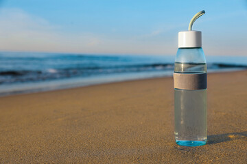 Glass bottle with water on wet sand near sea. Space for text