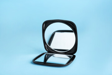 Stylish cosmetic pocket mirror on light blue background